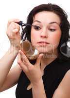 Woman is applying mascara while looking in mirror