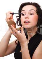 Woman is applying mascara while looking in mirror