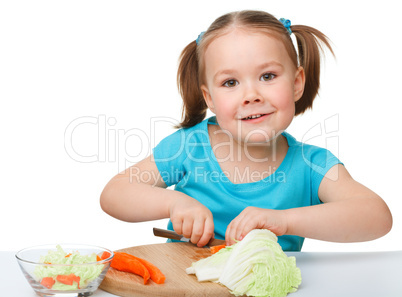 Little girl is cutting carrot for salad