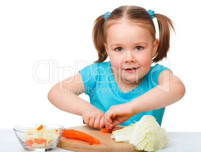 Little girl is cutting carrot for salad