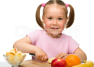 Little girl is cutting fruits for salad