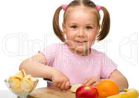 Little girl is cutting fruits for salad
