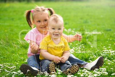 Two children are sitting on green meadow