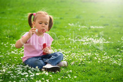 Little girl is sitting on green meadow