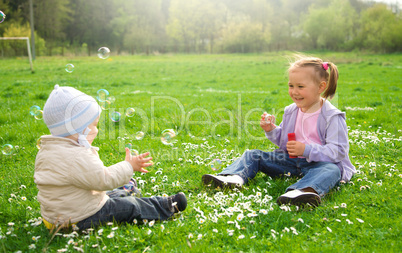 Two children are sitting on green meadow