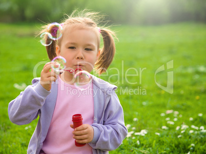 Little girl blows soap bubbles on meadow