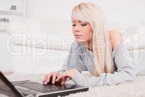 Attractive blond woman relaxing on laptop lying on a carpet