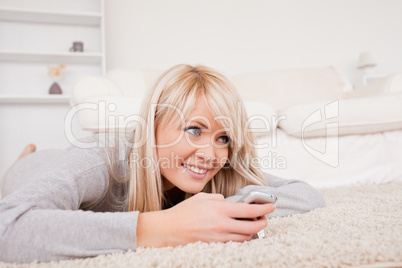 Pretty blond woman playing with cell phone lying down on a carpe