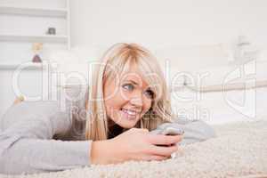 Pretty blond woman playing with cell phone lying down on a carpe