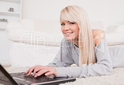 Pretty blond woman relaxing on laptop lying on a carpet