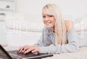 Pretty blond woman relaxing on laptop lying on a carpet