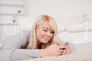 Attractive blond woman writing a text on cell phone lying down o
