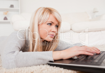 Beautiful concentrated woman relaxing on laptop lying on a carpe