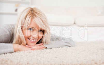 Charming blond woman posing lying down on a carpet