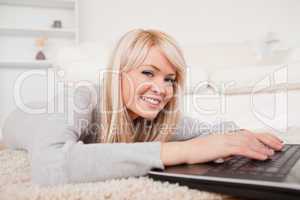 Beautiful blond woman relaxing on laptop lying on a carpet