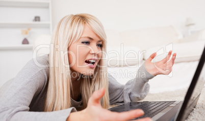 Beautiful blond woman frustrated with her computer lying on a ca