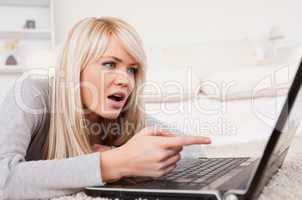 Pretty blond woman frustrated with her computer lying on a carpe