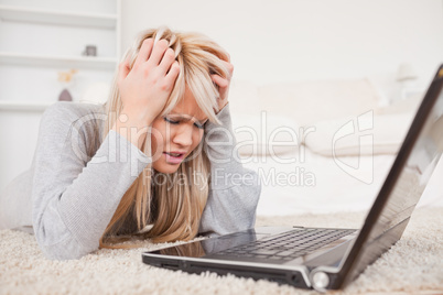 Attractive blond woman angry with her computer lying on a carpet