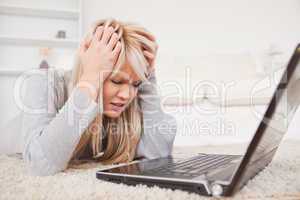 Attractive blond woman angry with her computer lying on a carpet