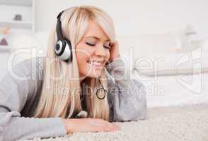 Prettyl blond woman with headphones lying on a carpet