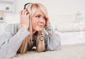 Beautiful blond woman with headphones lying on a carpet