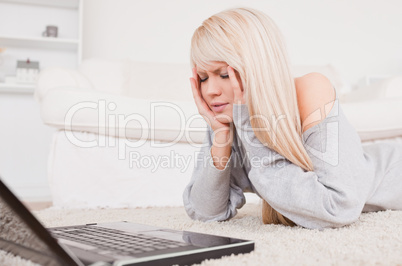 Pretty concentrated woman relaxing on laptop lying on a carpet