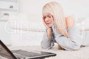 Pretty concentrated woman relaxing on laptop lying on a carpet