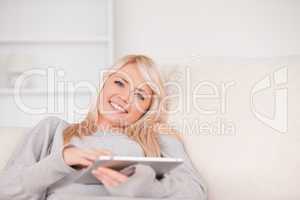 Pretty blond woman lying on a sofa relaxing on a line of tablet