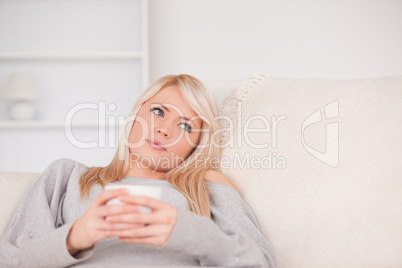Attractive blond woman lying on a sofa relaxing on a line of tab