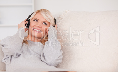 Beautiful blond woman with headphones lying in a sofa