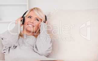 Beautiful blond woman with headphones lying in a sofa