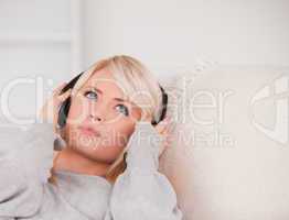 Attractive young blond woman with headphones lying in a sofa