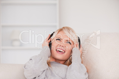 Beautiful young blond woman with headphones lying in a sofa