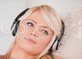 Attractive happy blond woman with headphones lying in a sofa