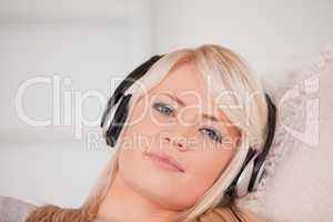 Beautiful happy blond woman with headphones lying in a sofa