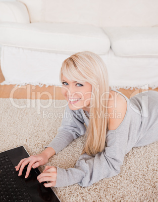 Attractive young blond woman relaxing on laptop lying on a carpe