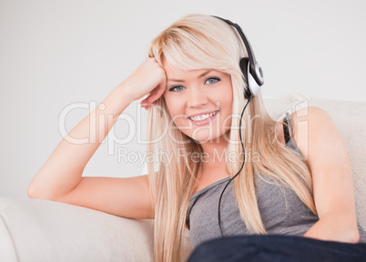 Attractive young blond woman with headphones sitting in a sofa
