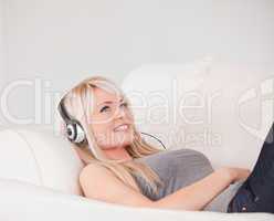 Happy young blond woman with headphones lying in a sofa