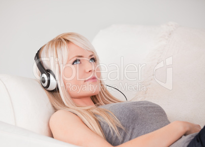 Attractive young blond woman with headphones lying in a sofa