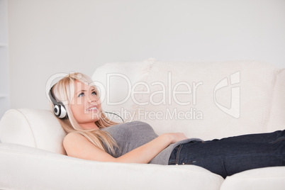 Smiling young blond woman with headphones lying in a sofa