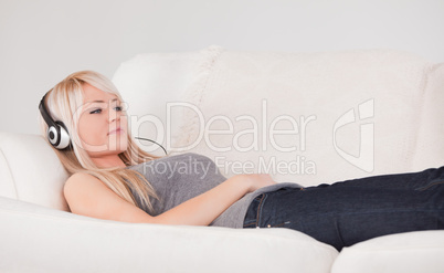 Glad young blond woman with headphones lying in a sofa