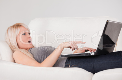 Surprised woman relaxing on laptop lying on a sofa