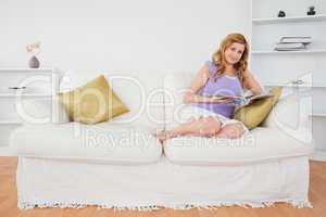 Pretty red-haired woman reading a magazine and posing while sitt