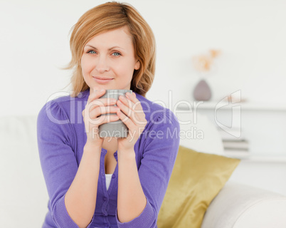 Charming red-haired woman holding a cup of coffee and posing whi