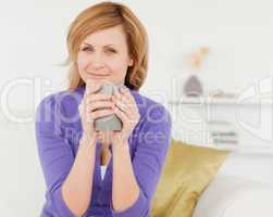 Charming red-haired woman holding a cup of coffee and posing whi