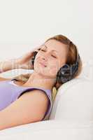 Happy blond-haired woman listening to music lying on the sofa