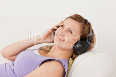 Smiling blond-haired woman listening to music lying on the sofa