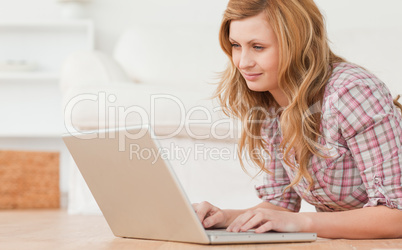 Blond-haired woman working on her laptop lying down on the floor