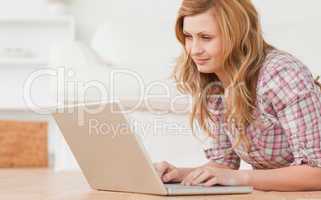 Blond-haired woman working on her laptop lying down on the floor