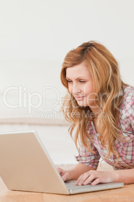 Blonde woman working on her laptop lying down on the floor